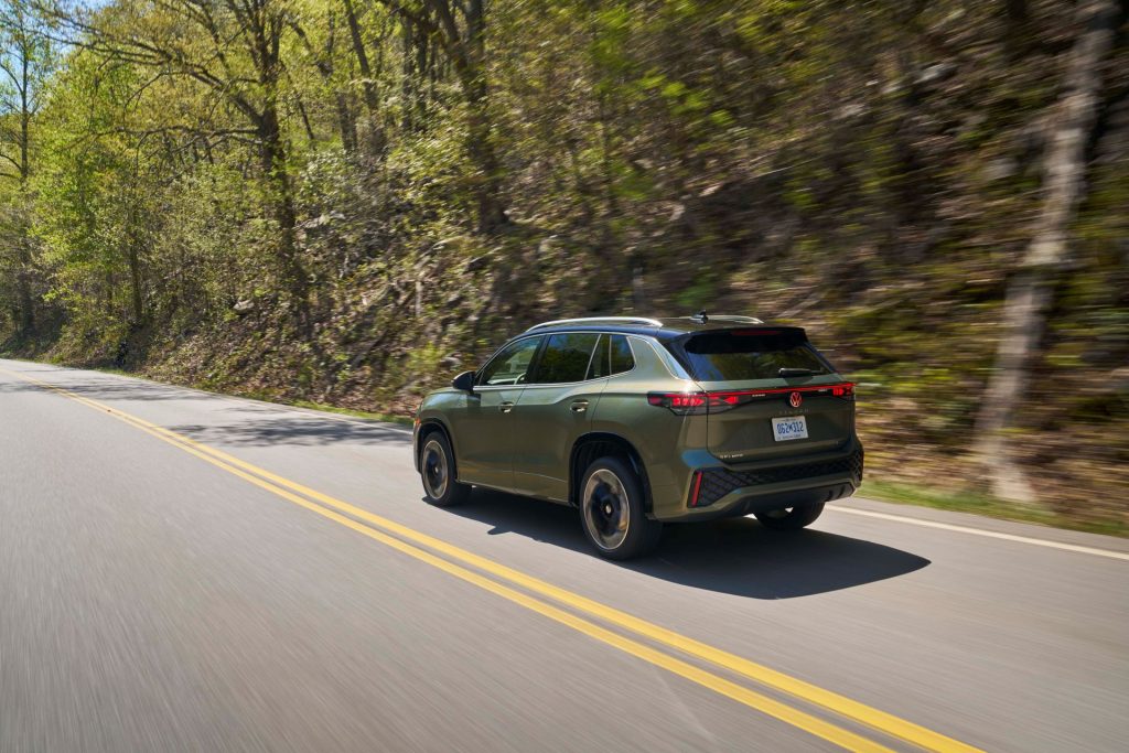 The Dark Green Back Exterior Of The 2026 Volkswagen Tiguan, Passing High Hills With Greenery And Trees